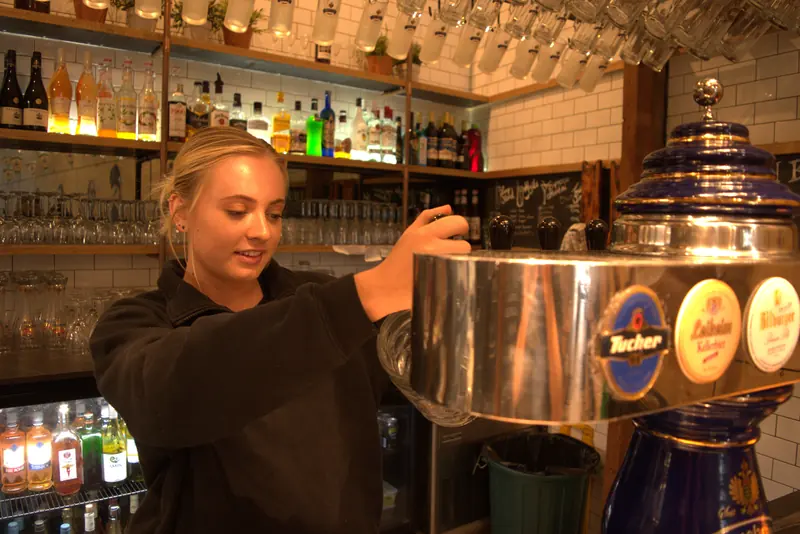 Bartender pouring a beer from the tap tower in front of a wall of spirits
