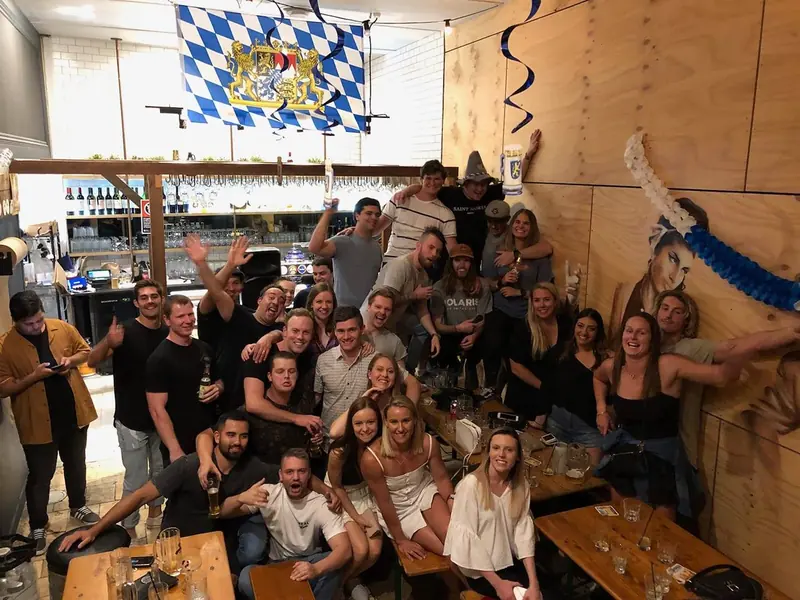 A big group of friends posing together inside the beerhall beneath a Bavarian flag