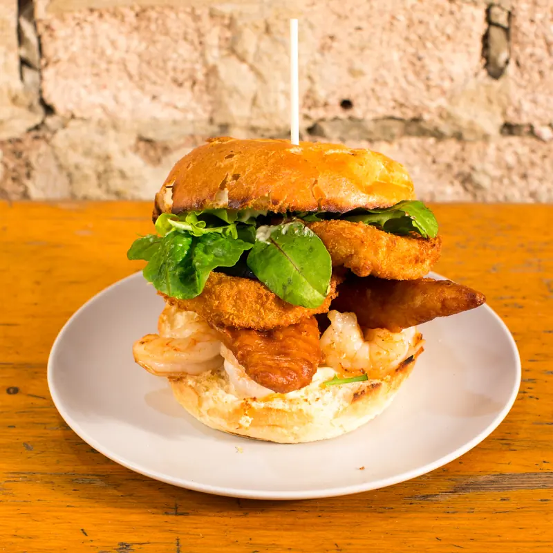 Tall burger stacked with crumbed seafood, rocket and sauce
