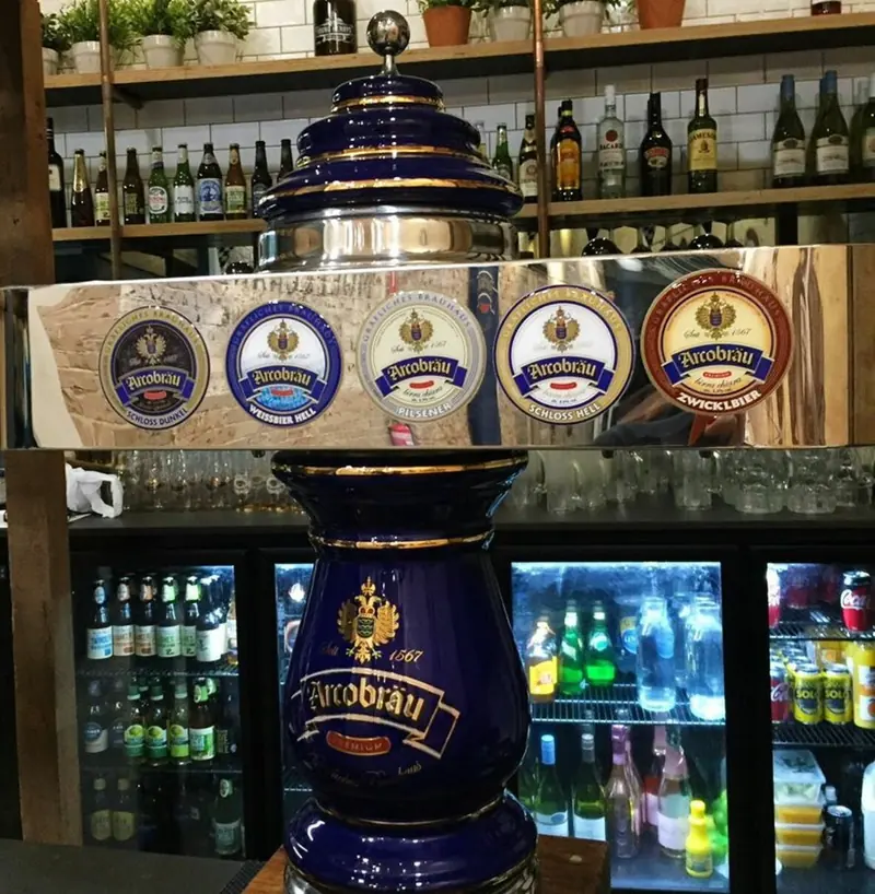 Ornate blue ceramic beer tap tower with a row of German beer badges above the bar